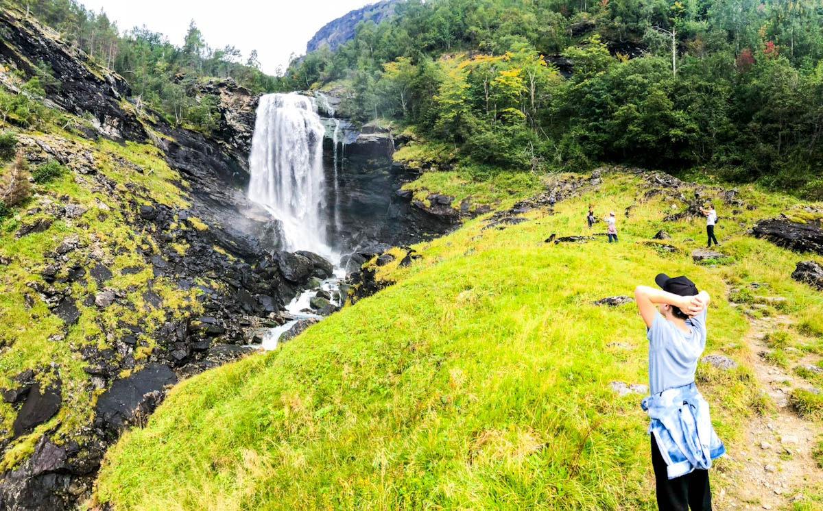 Boy looking at a waterfall in Norway with hands on head